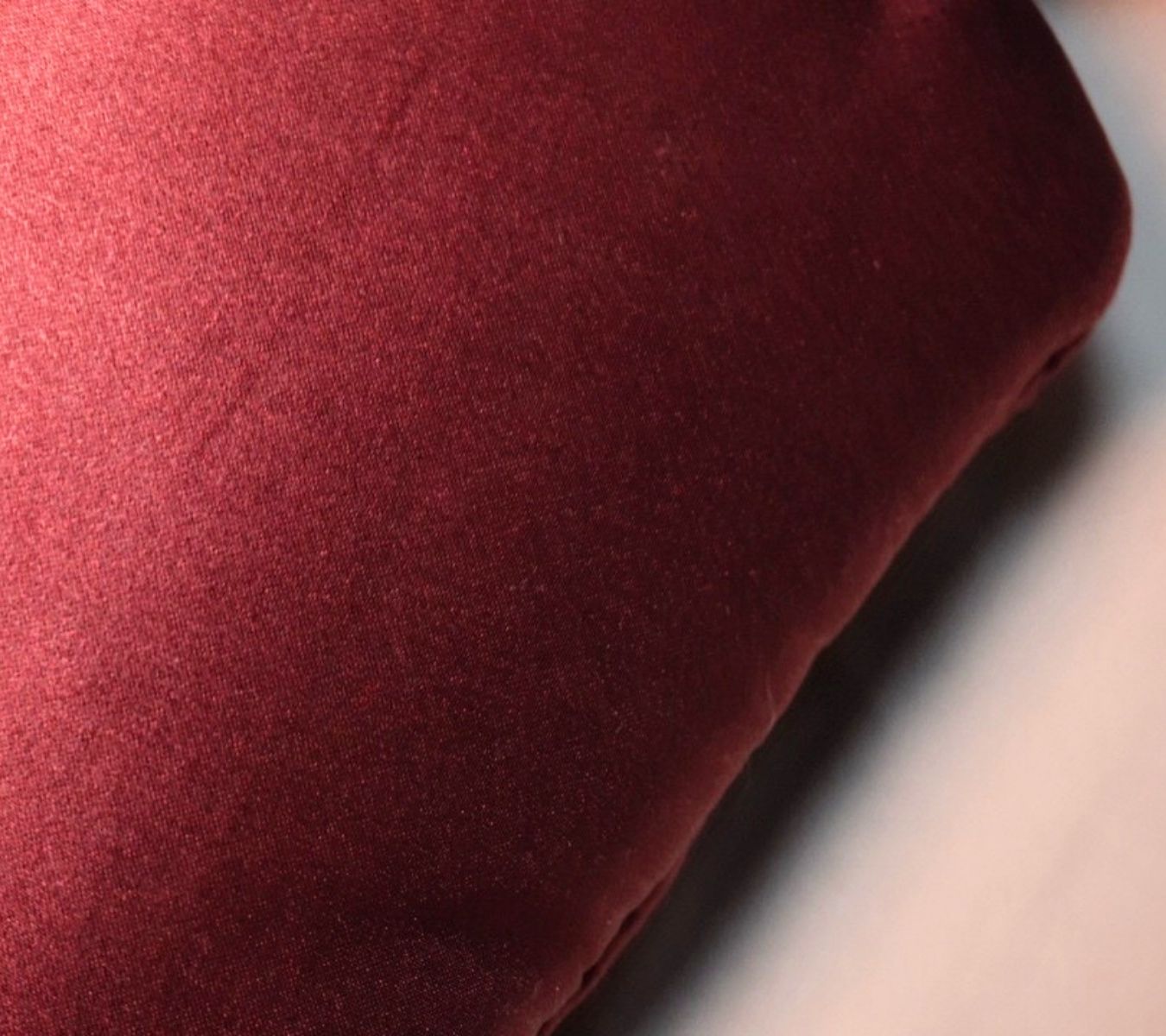 A close-up of a deep burgundy silk sleep mask texture, showing the soft sheen and folds of the material.