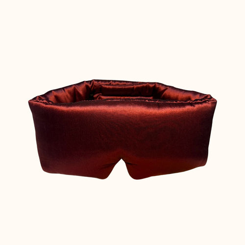 A plush, padded silk eye mask in a deep burgundy, shown against a plain off-white background.
